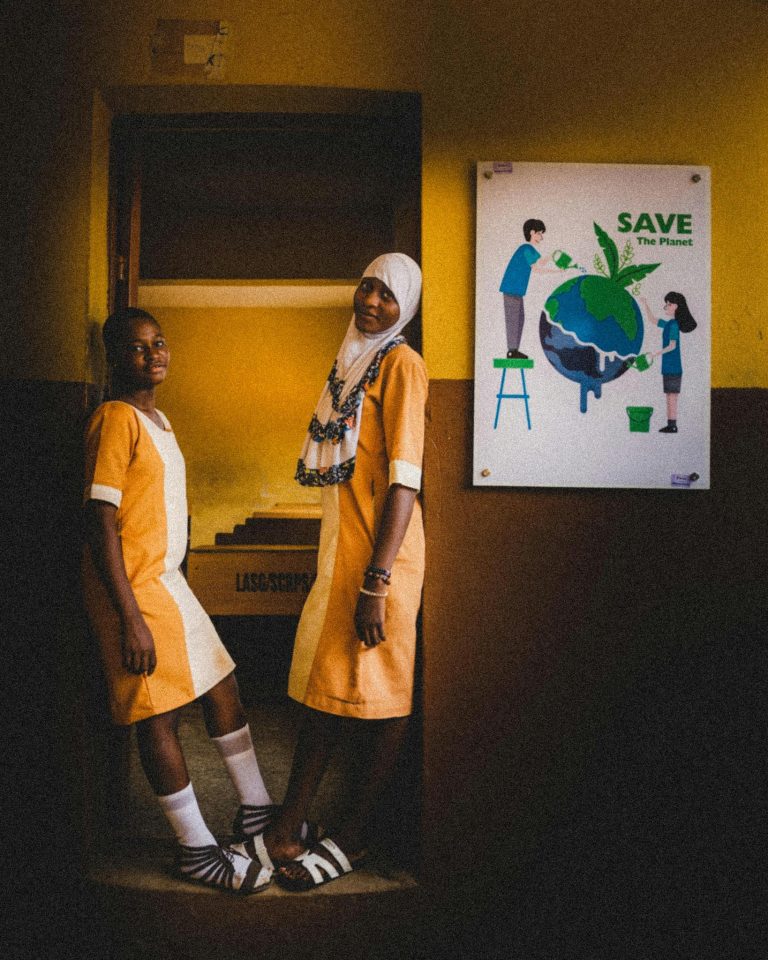 Two students in uniform stand by a Save the Planet poster indoors.