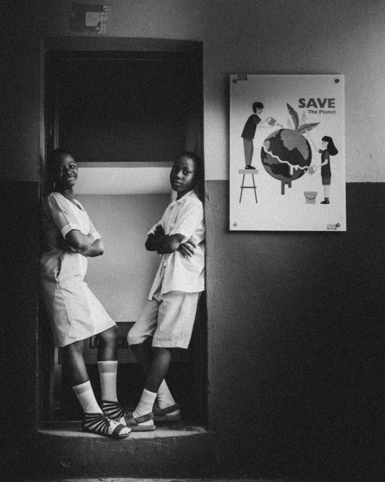 Two students pose in school setting next to 'Save the Planet' poster.